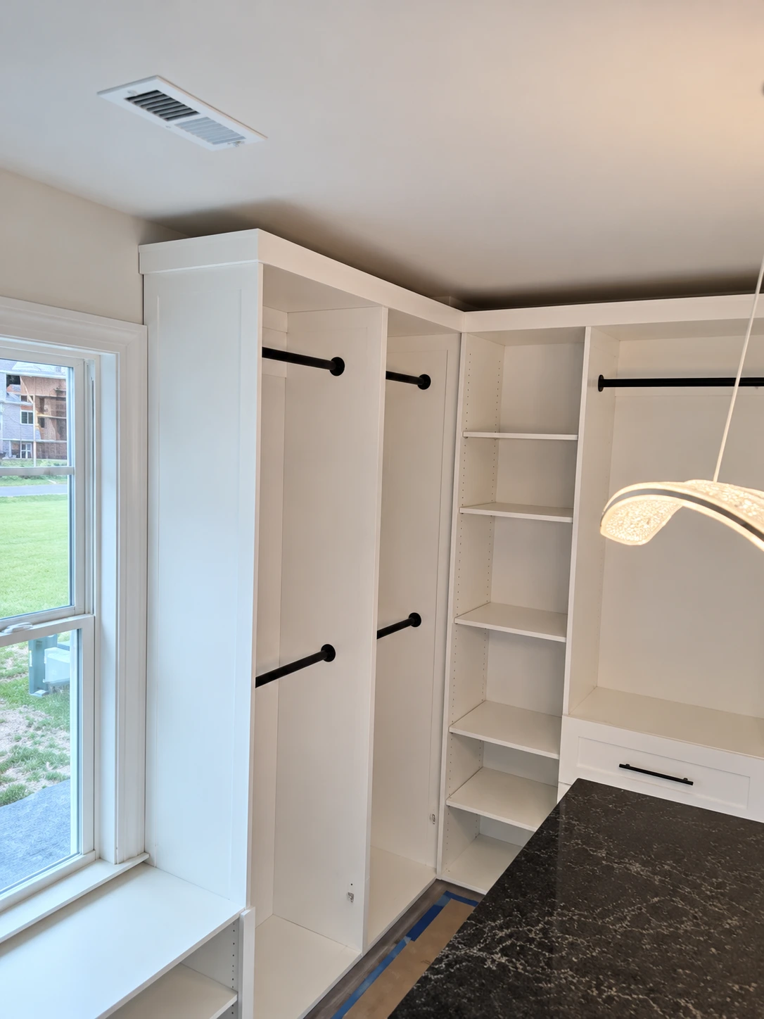 Empty walk-in closet with white shelving, black rods, and glass door with exterior view