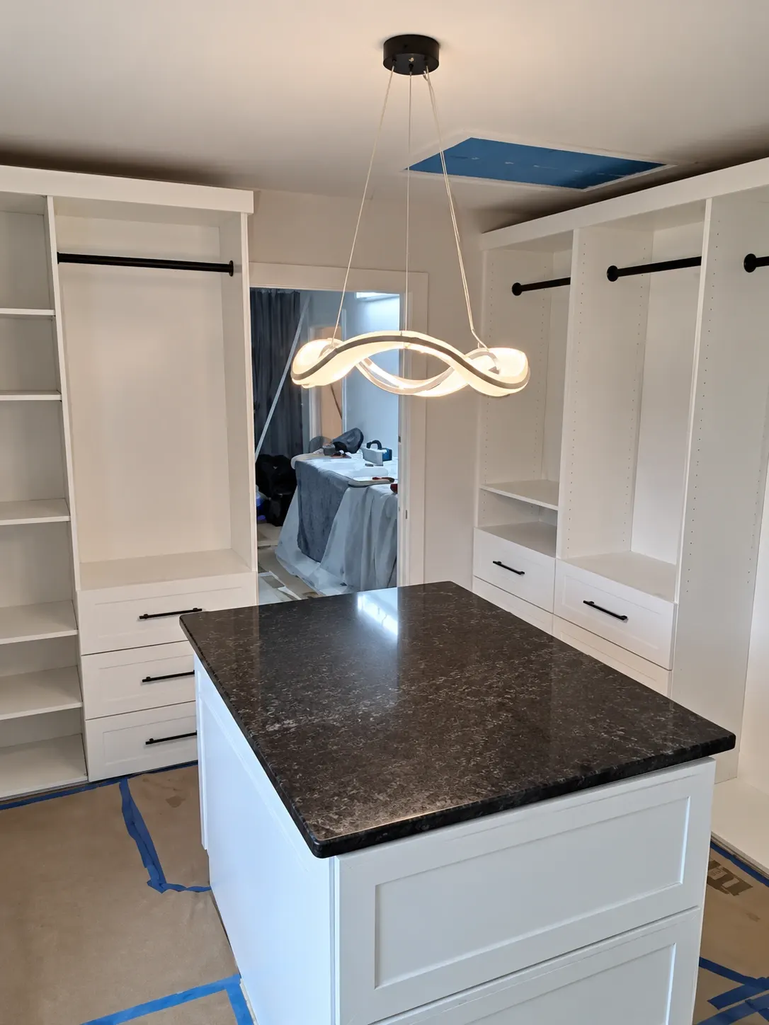 Modern walk-in closet with white cabinetry, dark countertop island, and curved pendant light